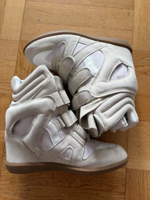 Isabel marant skor - Unika beige sneakers med högt skaft och coola paneler i mocka och textil. Skorna har flera breda kardborreband och en brun gummisula. Perfekt för dig som vill sticka ut med en futuristisk vibe och bekväm passform.
