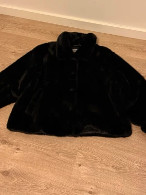 Svart pälsjacka från Hollies - Snygg svart pälsjacka från Hollies i modellen NAP. Jackan har en klassisk krage, knäppning framtill och är gjord i mjuk fuskpäls som känns lyxig och varm. Perfekt för kalla vinterdagar och ger en trendig look till din outfit.