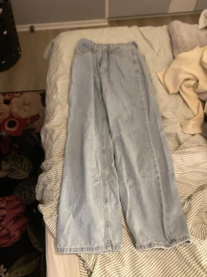 Ljusa wide leg jeans med rosa broderi - Säljer ett par ljusa wide leg jeans med cool passform och rosa broderade rosetter på bakfickorna. Jeansens material är klassisk denim och de har en avslappnad look som är perfekt för dig som gillar trendiga och bekväma kläder.