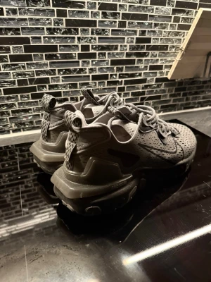 Nike grå sneakers med svart mönster - Säljer ett par grå Nike sneakers med svart mönster och tydlig swoosh på sidan. Skorna har en chunky sula med detaljer och snörning framtill. Perfekt för dig som gillar sportig stil.