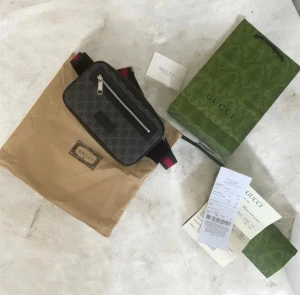 Gucci axelväska i svart monogram - Snygg axelväska från Gucci i svart med klassiskt GG-monogrammönster. Väskan har en silverfärgad dragkedja framtill och justerbar axelrem med röda och svarta detaljer. Materialet är canvas med läderdetaljer. Perfekt för dig som vill ha en trendig och praktisk väska.