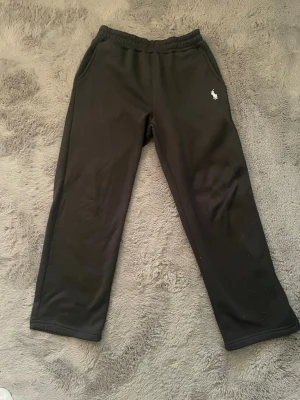 Svarta och vita mjukisbyxor från Polo - Två par mjukisbyxor från Polo Ralph Lauren, ett par svarta och ett par vita. Byxorna har raka ben, elastisk midja och sidofickor. Diskret Polo-logga broderad på höften. Perfekta för chill och avslappnade dagar.
