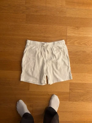 Vita shorts med snörning - Säljer ett par vita shorts med snörning i midjan och fickor på sidorna. Shortsen har en bakficka och är tillverkade i mjukt material, perfekta för sommardagar. Enkel och clean design som passar till det mesta.