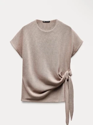 Beige topp med knyt från Zars - Säljer en beige topp från Zara med korta ärmar och rund hals. Toppen har en snygg knytdetalj i sidan som ger en unik look. Perfekt att styla med jeans eller kjol för en trendig outfit.