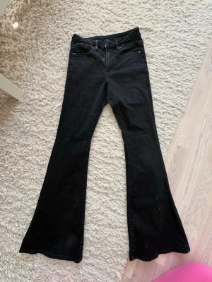 Svarta bootcut jeans - Säljer ett par svarta bootcut jeans med hög midja och klassisk femficksdesign. Jeansen har utsvängda ben och är tillverkade i ett stretchigt denimtyg som sitter snyggt. Perfekta för dig som gillar en retroinspirerad look.