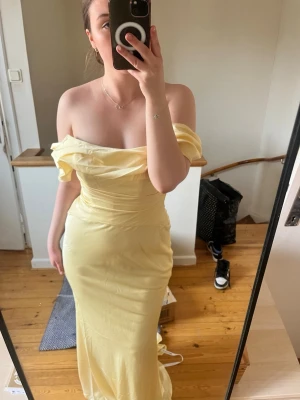 Ljusgul offshoulder långklänning - Elegant ljusgul långklänning med offshoulder-design och figurnära passform. Klänningen har en vacker drapering över bysten och en dragkedja i ryggen. Säljer då den va för stor!
