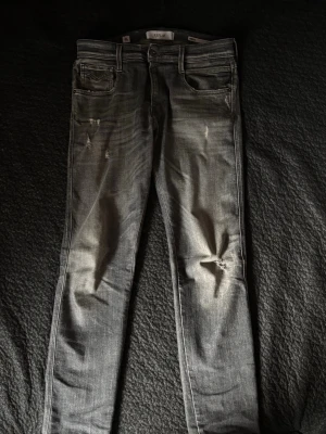 Replay Anbass  - Säljer ett par grå jeans från Replay med slitningar på framsidan och klassiska femficksdetaljer. Jeansen har en slim fit och är tillverkade i denim med snyggt tvättad look. Perfekta för dig som gillar en cool och avslappnad stil. Strl 30/32 hör av dig vid frågor