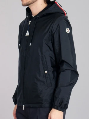 Svart vindjacka från Moncler - Stilren svart vindjacka från Moncler med huva och dragkedja framtill. Jackan har två snedställda fickor med tryckknappar, elastiska muddar vid ärmslut och nederkant samt Moncler-logga på ärmen. Materialet är glansigt och lätt, perfekt för blåsiga dagar.