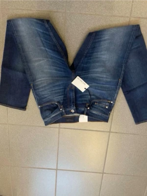 Blå jeans från tiger of sweden Jeans - Snygga blå jeans från tiger of sweden Jeans med klassisk femficksmodell och raka ben. Jeansen har en tvättad look med ljusare partier och kontrastsömmar. Tillverkade i slitstarkt denimtyg, perfekta för en avslappnad stil.