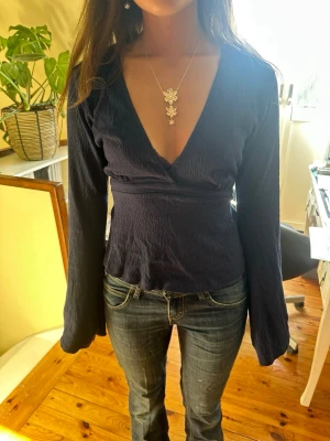 Marinblå blus med v-ringning - Snygg mörkblå topp med djup v-ringning och långa ärmar. Toppen har en markerad midja med snörning för en smickrande passform. Perfekt till sommaren. Skriv vid funderingar. Godkänner snabba prisförslag!