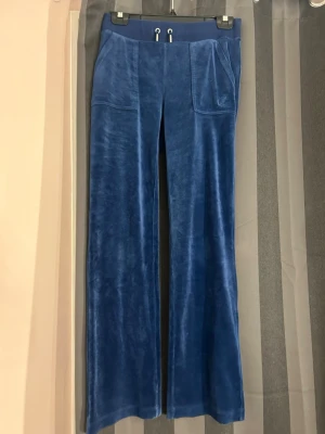 mörkBlå velour mjukisbyxor Juicy Couture -  mörkBlå mjukisbyxor i velour från Juicy Couture med bred resår i midjan och dragsko. Byxorna har raka ben, stora fickor fram och bakfickor med knapp. Perfekta för en chill och trendig look.