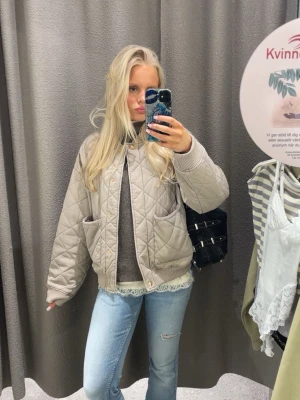 Beige vårjacka - Quiltad bomberjacka i beige från H&M med ribbade muddar vid ärmslut, krage och nederkant. Jackan har två stora framfickor och stängs med tryckknappar. 