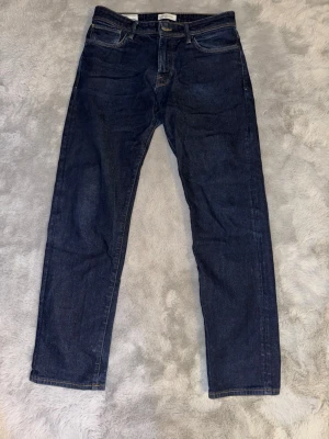 Mörkblå raka jeans herr - Snygga mörkblå jeans från selected homme med rak passform och klassisk femficksdesign. Jeansen har normal midja och är tillverkade i ett slitstarkt denimtyg. Perfekta för en stilren och enkel look. Liten defekt vid dragkedjan.