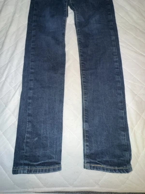 Blå raka jeans i klassisk modell - Säljer ett par blå jeans med rak passform och normal midja. Jeansen har en klassisk femficksdesign och är tillverkade i denim. Perfekta för dig som gillar en enkel och tidlös stil.