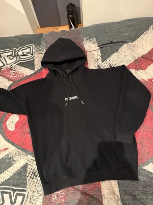 Svart hoodie från FSBN med tryck - Svart hoodie från FSBN med vit text 'F*CK OFF.' på bröstet. Klassisk modell med huva, dragsnören och stor magficka. Perfekt för dig som gillar en chill och edgy stil. Materialet är mjuk bomullsmix som känns skön mot huden.