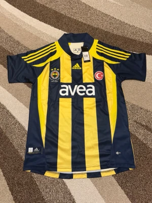 Fenerbahce 07-08 Hemmatröja  - Säljs av ICEKIT  Storlek: M Namn + nummer: Alex #10 Badge: Ingen  Här kan du se tröjor i ICEKIT Outlet. Alla tröjor är helt nya och utan några problem. Du kan välja att köpa dem här eller direkt via vår hemsida.  Tröjorna finns tillgängliga hos ICEKIT på: https://www.icekit.se  Länk: https://www.icekit.se/collections/outlet
