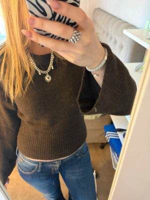 Mörkbrun stickad tröja med vida ärmar - Mysig mörkbrun stickad tröja med rund hals och vida ärmar. Tröjan är figurnära med ribbstickad nederkant och ärmslut. Perfekt för lager-på-lager och passar till jeans eller kjol.