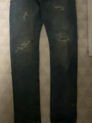 Jeans med slitningar från Jack and Jones  - Säljer ett par blå jeans med slitningar på låren och knäna. Jeansen har klassisk femficksdesign och är gjorda i denim. Perfekta för en avslappnad och trendig look.