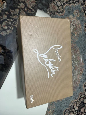 Christian Louboutin skokartong - Säljer en original skokartong från Christian Louboutin Paris med tillhörande vit dustbag med röd logotyp. Perfekt för dig som vill förvara eller presentera dina exklusiva skor på ett snyggt sätt.