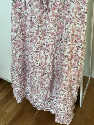 Långkjol med rosa blommor - Jättefin söt rosa långkjol. Kjolen är luftig och skön med snörning vid midjan. Den går ner till anklarna 