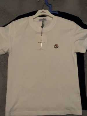 Moncler t-shirt i vitt och svart - Två Moncler t shirts, en vit och en svart,. Båda har Moncler-loggan broderad på bröstet och är tillverkade i mjuk bomull. Perfekt för dig som gillar stilrena basics med exklusiv känsla. Påse och kartong medföljer en för 700 eller 2 för 1200 