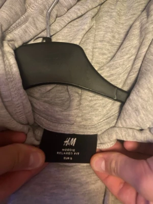 Grå hoodie  - En enkel och stilren grå hoodie från H&M med relaxed fit. Hoodien har huva med dragsko, ribbade muddar och en stor magficka. Perfekt för dig som gillar en avslappnad look. Materialet är mjukt och bekvämt, troligtvis bomullsblandning.