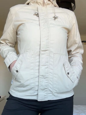 Beige Vårjacka - Beige vårjacka med huva. 4 fickor + 2 innerfickor. Stängs med dragkedja och kardborre (3 av de sitter halvt löst, men går att stänga ändå!) Storleken är S men passar på M & XS om lite overzised känsla är önskad! 🤍 PRIS GÅR ATT DISKUTERA.
