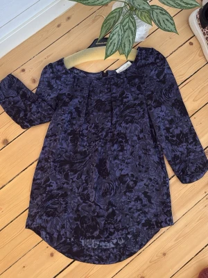 Mörkblå blommig blus från By Malene Birger - Snygg mörkblå blus med blommigt mönster från By Malene Birger. Blusen har trekvartsärm och rund halsringning med lätt rynk framtill. Tunt, flowy material som ger en avslappnad men stilren look.