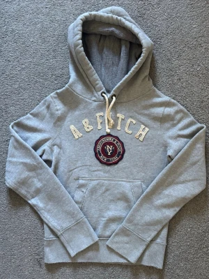 Vintage Abercrombie & Fitch Hoodie - As Snygg vintage  grå hoodie från Abercrombie & Fitch med broderad logga och text på bröstet. | Storlek S | Längd 64cm , Bredd Armhåla - Amrhåla 50cm | Mycket fint skick | Pris kan diskuteras! Modell 175 cm, 68kg