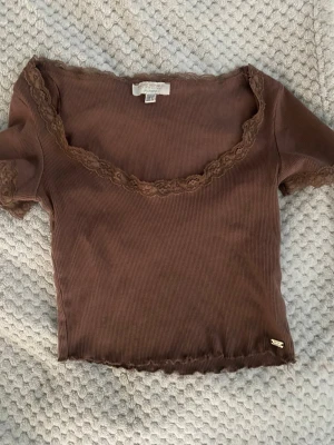 Brun topp - Söt brun ribbad topp med korta ärmar och spetsdetaljer vid halsringning och ärmslut. Modellen är croppad. Köpt i Spanien för flera år sen.