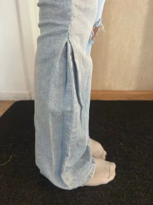 Ljusblå bootcut jeans Gina Tricot - Ljusblå jeans med bootcut passform och slitningar på båda benen. Jeansen har klassisk femficksdesign, knapp och dragkedja framtill samt en cool slits på sidan av benen. Perfekta för dig som gillar en avslappnad och trendig look. Från Gina Tricot Young storlek 158.