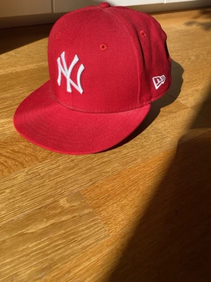 Röd New Era NY Yankees keps - Snygg röd keps från New Era, modell 59FIFTY, med klassiskt NY Yankees broderi i vitt framtill. Kepsen har rak skärm och broderade ventilationshål. Perfekt accessoar för en sportig och trendig look.