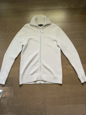Riktigt schysst ziptröja från Brand Island - Snygg beige ziptröja från Brand Island med hög ribbad krage och hel dragkedja framtill. Tröjan har långa ärmar och ribbade muddar vid ärmslut och nederkant. Perfekt för lager på lager och enkel att matcha till olika outfits.