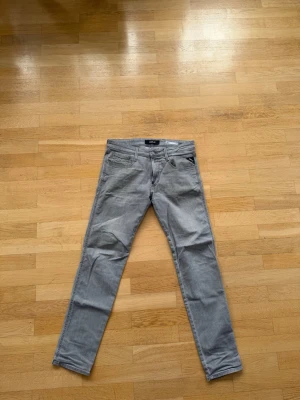 Grå slim fit jeans från Replay - Snygga grå jeans från Replay i modellen Anbass. Slim fit med klassisk femficksdesign och dragkedjegylf. Jeansen har en diskret tvättad look och Replay-logga på fickan. Perfekta för en trendig och avslappnad stil.