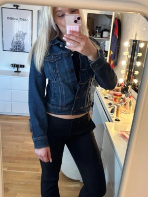 Mörkblå jeansjacka med klassisk passform - Snygg mörkblå jeansjacka med figurnära passform och klassiska sömmar. Jackan har bröstfickor med lock och knappar framtill. Perfekt att slänga över en t-shirt eller hoodie för en cool look.