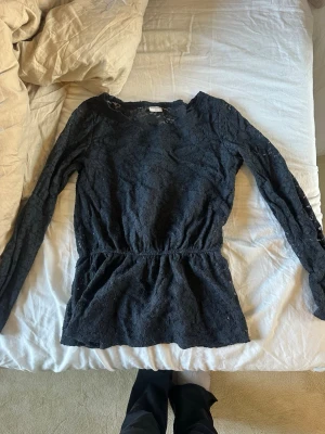 Marinblå spetsblus med lång ärm - Marinblå blus i spets med lång ärm och markerad midja. Blusen har ett transparent blommigt spetsmönster och är perfekt för dig som gillar en feminin och trendig stil. Snygg att styla med både jeans och kjol.