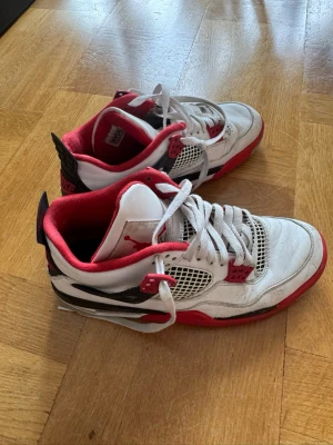 Nike Air Jordan 4 Fire Red sneakers - Säljer ett par Nike Air Jordan 4 Fire Red sneakers med vit ovandel, röda och svarta detaljer samt meshpaneler på sidorna. Skorna har klassisk Jordan-logga på plösen och synlig Air-enhet i sulan. Perfekta för dig som gillar retrostil och streetwear. Storlek 42 använt skick.