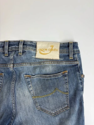 Blå jeans från Jacob Cohen - Snygga blå jeans från Jacob Cohen med klassisk femficksdesign och gul kontrastsöm. Jeansen har en rak passform och är tillverkade i mjuk denim med en lätt tvättad look. Perfekta för en avslappnad och trendig stil.