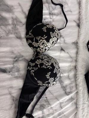 Svart push-up bh med spetsdetaljer - Snygg svart push-up bh med vadderade kupor och vacker blommig spets i beige ovanpå. Bh:n har justerbara axelband och klassisk knäppning bak. Perfekt för dig som gillar en feminin och elegant stil. Inga defekter, varsamt använd. Stl 80B från Lindex modellen MALVA. Bara höra av dig vid frågor💕