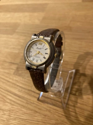 Vintage Rachel Quartz Armbandsur - Ett Rachel Quartz armbandsur med ett brunt läderarmband. Urtavlan är vit med romerska siffror och guldiga detaljer. Boetten är i rostfritt stål. Klockan har ett japanskt urverk. Fint skick enligt bilder, behöver bara nytt batteri.  Begagnat värde: < 500 SEK Mitt pris: 189 SEK  Skickas alltid snabbt och spårbart. Skriv vid frågor och se gärna mina andra annonser!   GRATIS: För återkommande kunder erbjuder jag personlig experthjälp för dig att göra nya fynd (nytt & begagnat). Fråga för mer info!