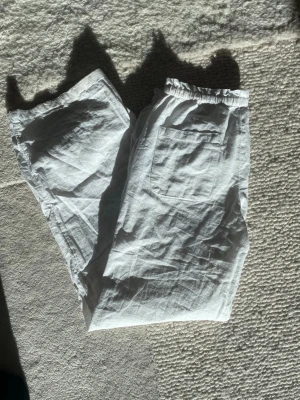 Vita linnebyxor med resårmidja - Säljer ett par vita linnebyxor med avslappnad passform och resår i midjan. Byxorna har dragsko och en bakficka, perfekta för en chill och luftig stil. Materialet är 100% linne vilket gör dem svala och bekväma. Byxorna är nu lite för små för mig så det är därför jag inte vill ha de längre😜