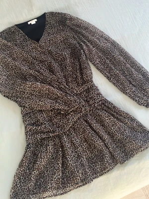 Leopardmönstrad kort klänning - Säljer en snygg kort klänning med leopardmönster och v-ringning. Klänningen har långa ärmar och markerad midja som ger en smickrande siluett. Perfekt för dig som vill sticka ut med ett djurmönster. Materialet känns lätt och luftigt.