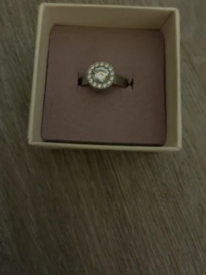 Silverfärgad ring med gnistrande stenar - Stilren silverfärgad ring med rund form och en större klar sten i mitten, omgiven av mindre gnistrande stenar. Perfekt för dig som gillar bling och vill ha något som sticker ut på fingret. Ringen har en klassisk och elegant look. Den är aldrig använd köpt ifrån Edblad för 449kr men säljer den för 399 pris går alltid att diskutera 🤗ringen är i storlek xs 
