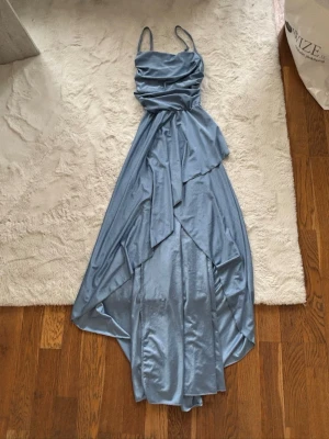 Ljusblå långklänning med drapering SHEIN 15Y - Elegant ljusblå långklänning med tunna axelband och vacker drapering framtill. Klänningen har en flytande siluett och är tillverkad i ett glansigt, mjukt material som ger en lyxig känsla. Perfekt för speciella tillfällen. Säljer då jag köpte den till min bal i 9an men den passade inte, pris kan diskuteras 
