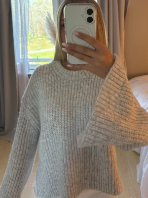 Ljusgrå oversized stickad tröja - Mysig ljusgrå stickad tröja med breda ärmar och ribbad struktur. Med slit i armar och midja.