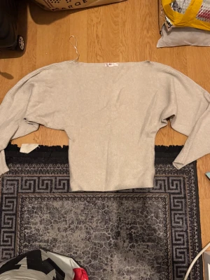 Beige stickad tröja - Beige  stickad tröja med bred halsringning och shoulder of passform. Tröjan har långa, vida ärmar och smal midja vilket ger en snygg siluett. Perfekt för dig som gillar en avslappnad men trendig stil.