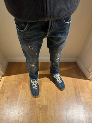 Dondup jeans - Säljer ett par mörkblå jeans med slitningar och vita kontrastsömmar. Jeansen har klassisk femficksdesign och en avslappnad passform. Perfekta för en cool och avslappnad stil.