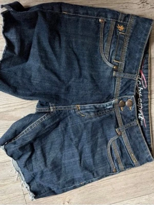 Lågmidjade Mörkblå jeansshorts - Snygga mörkblå jeansshorts från EDC by Esprit med kanter man kan vika upp och dubbla knappar framtill. Klassisk femficksmodell med dekorativa sömmar och broderad logga på bakfickan. Skit snygg passform och låg missade!!