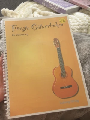 Första Gitarrboken av Bo Strömberg - En Gitarbok (för barn). Den är lite skrynklig utanpå (som på bild) då den har tillhört ett barn. Finns även sidor man kan göra sin egna låt med akord. Perfekt för nybörjare och barn som vill lära sig spela gitarr, med ackorddiagram, övningar och låtar.