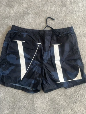 Valentino blå camo badbyxor - Riktigt feta Valentino badbyxor. 100% äkta, har även QR kod och sånt. De är lite slitna här och där och sen är snöret ur plats så lite svårt att knyta men om du inte behöver knyta så är det inga problem.